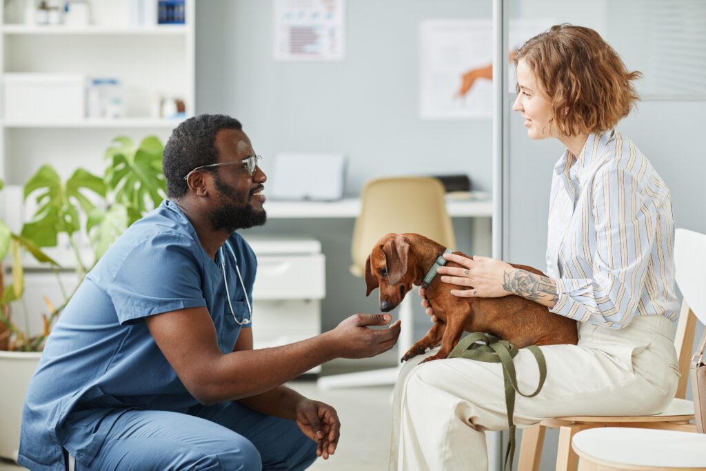 Female with dog in lap talks to kneeling veterinarian